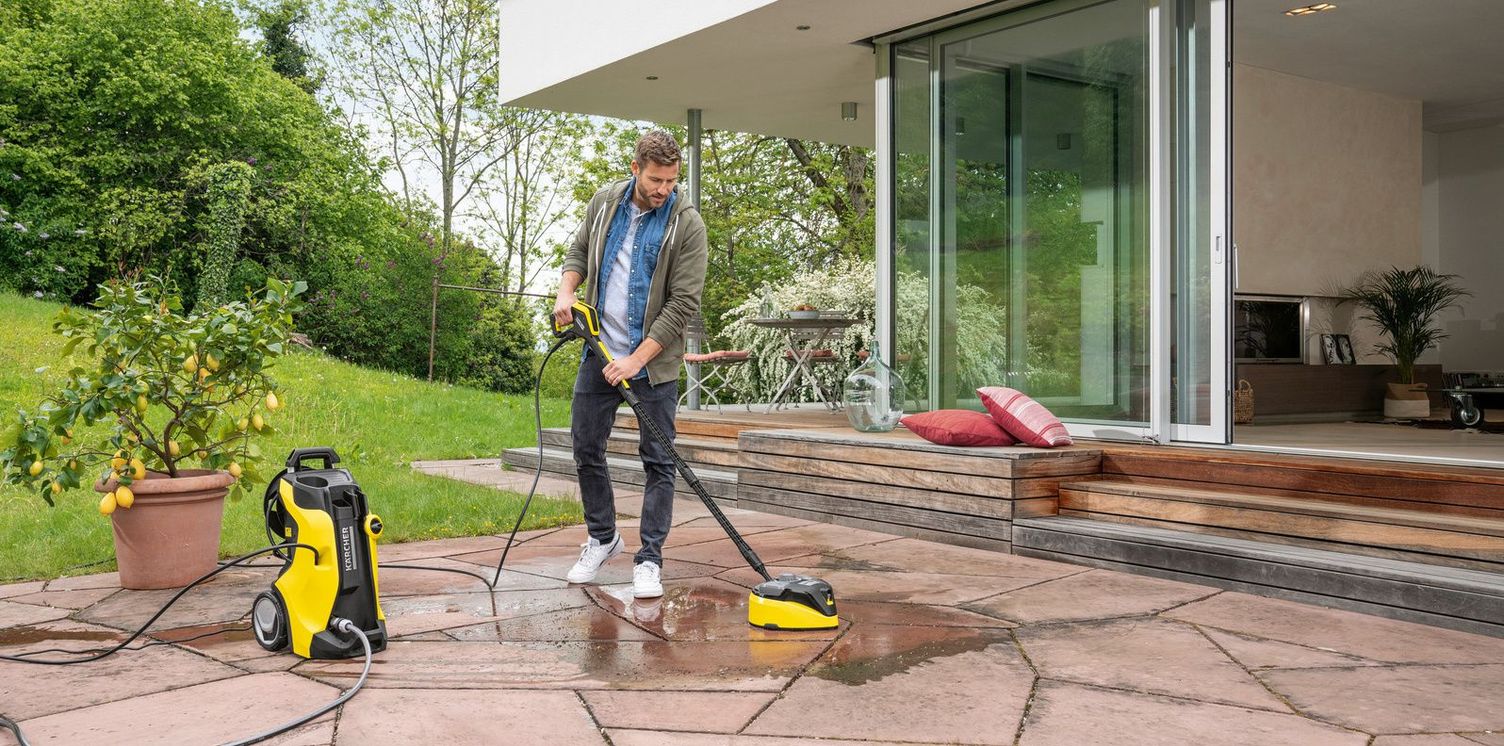 A man cleans his patio slabs with a Kärcher pressure washer and surface cleaning attachment