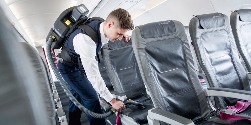 Person vacuuming plane seats with battery powered backpack vacuum cleaner Person vacuuming plane seats with battery powered backpack vacuum cleaner
