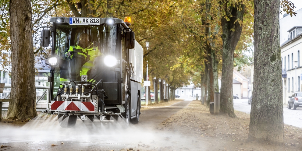 A person operating an implement carrier to clean a footpath