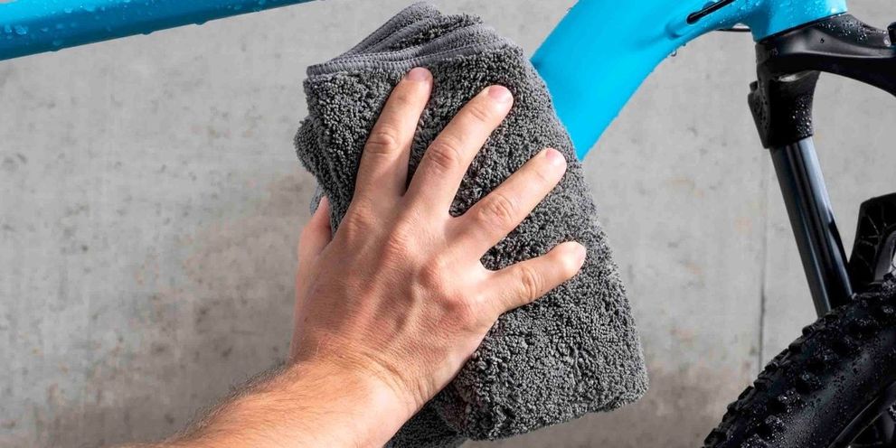 A light blue bike is dried with a cloth