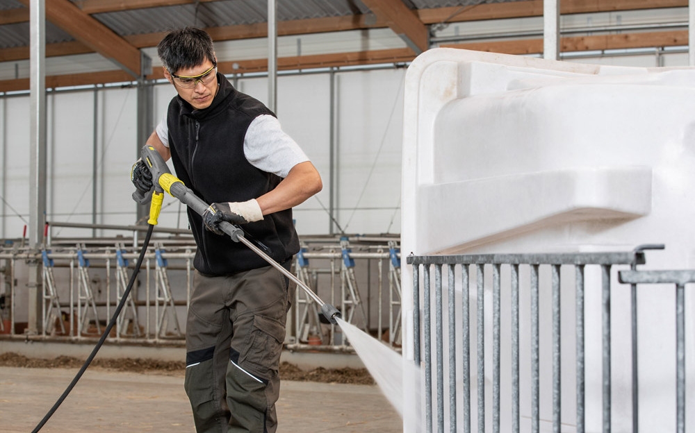 A worker cleans a calf hut with a Kärcher hot water pressure washer.