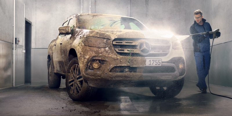 A worker pressure washes a car.