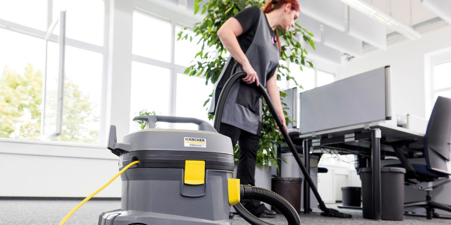 A worker uses a canister vacuum to clean office floors.