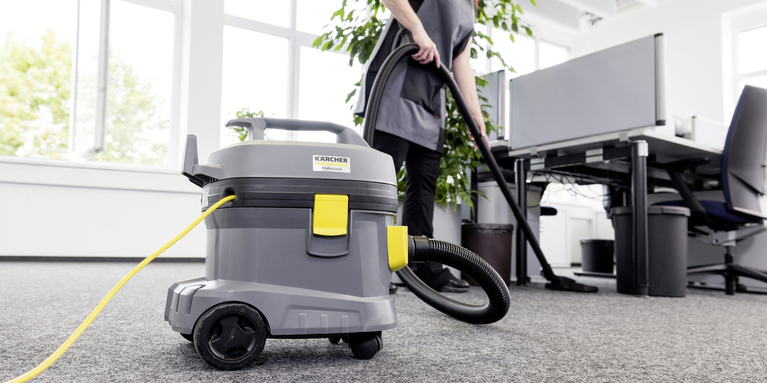 A worker vacuums carpet under cubicles in an office building.
