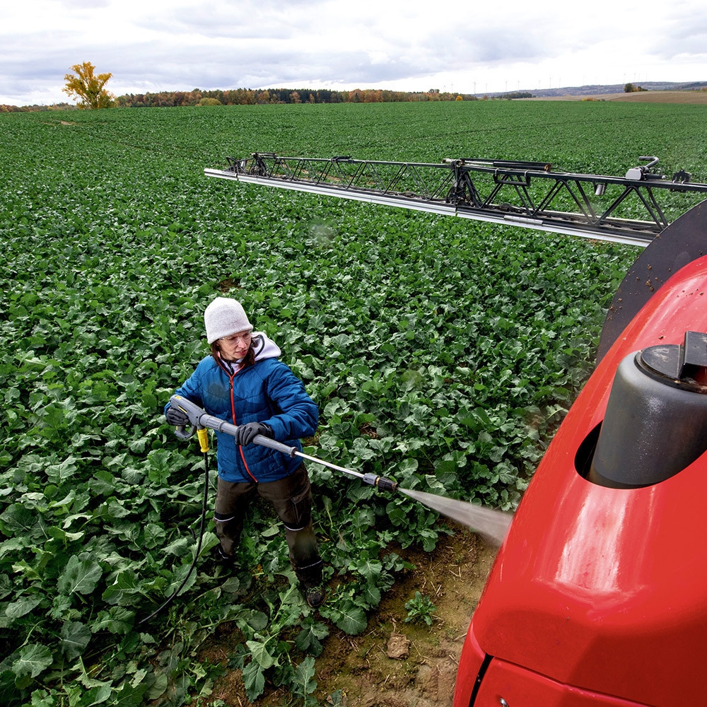 A worker cleans agriculture equipment in the field with a battery-powered cold water pressure washer.