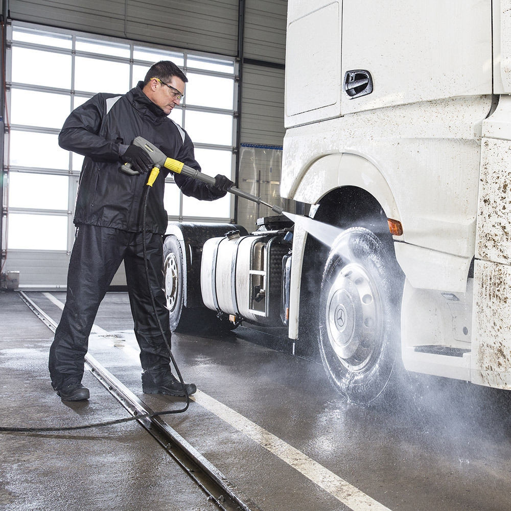 A worker pressure washes a semi truck cab with a cold water electric pressure washer.
