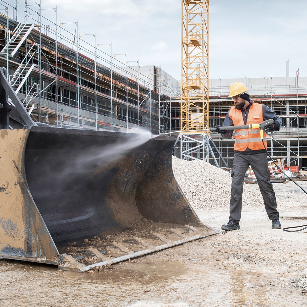 A worker cleans construction equipment with a gas-powered cold water pressure washer.