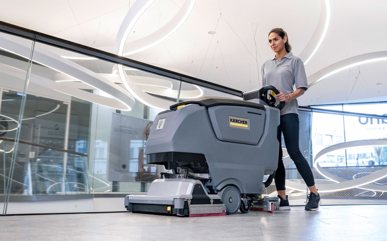 A worker cleans tiled flooring in a commercial space using a Kärcher commercial walk-behind floor scrubber.