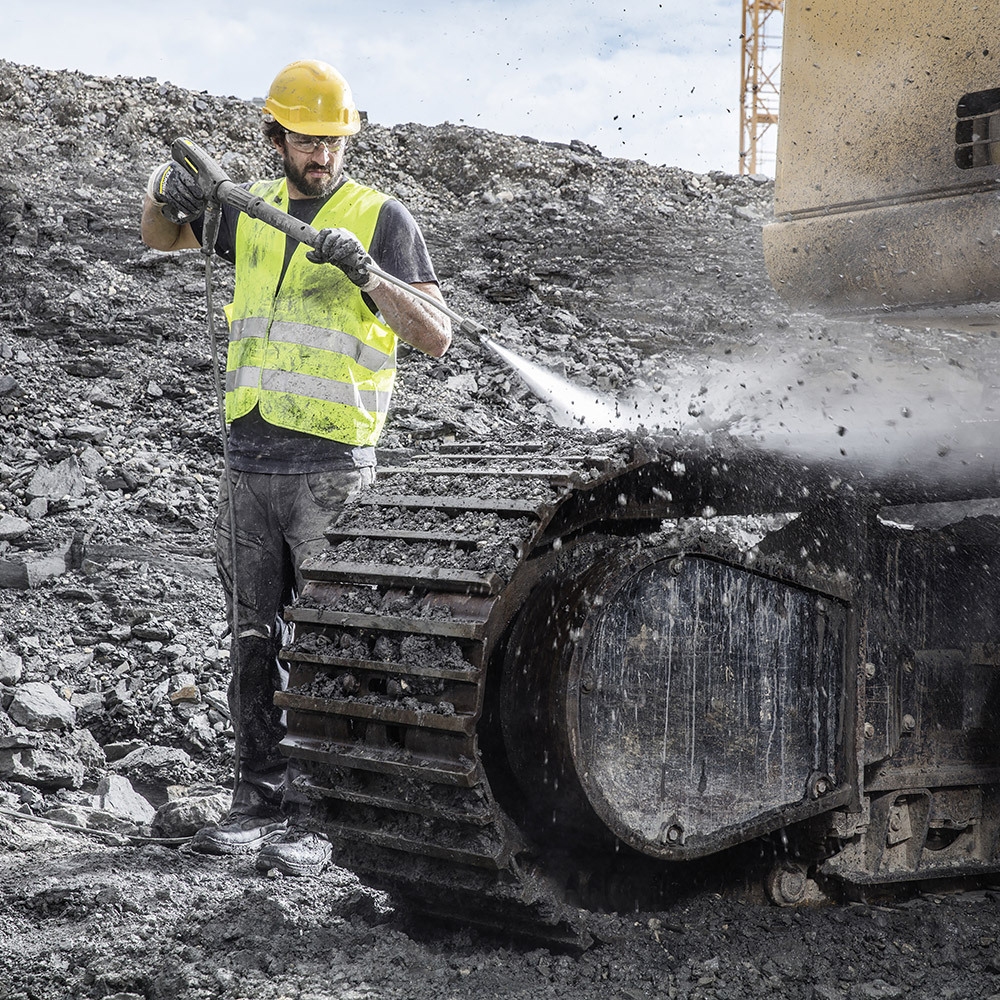 A worker pressure washes construction equipment with a gas-powered hot water pressure washer.