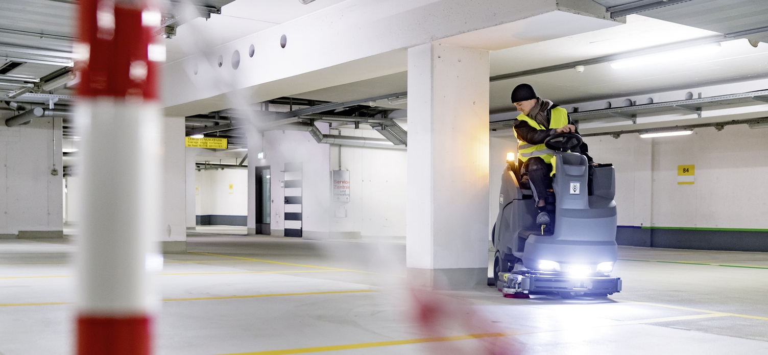A person is sitting on a ride-on sweeper and cleaning an airport area