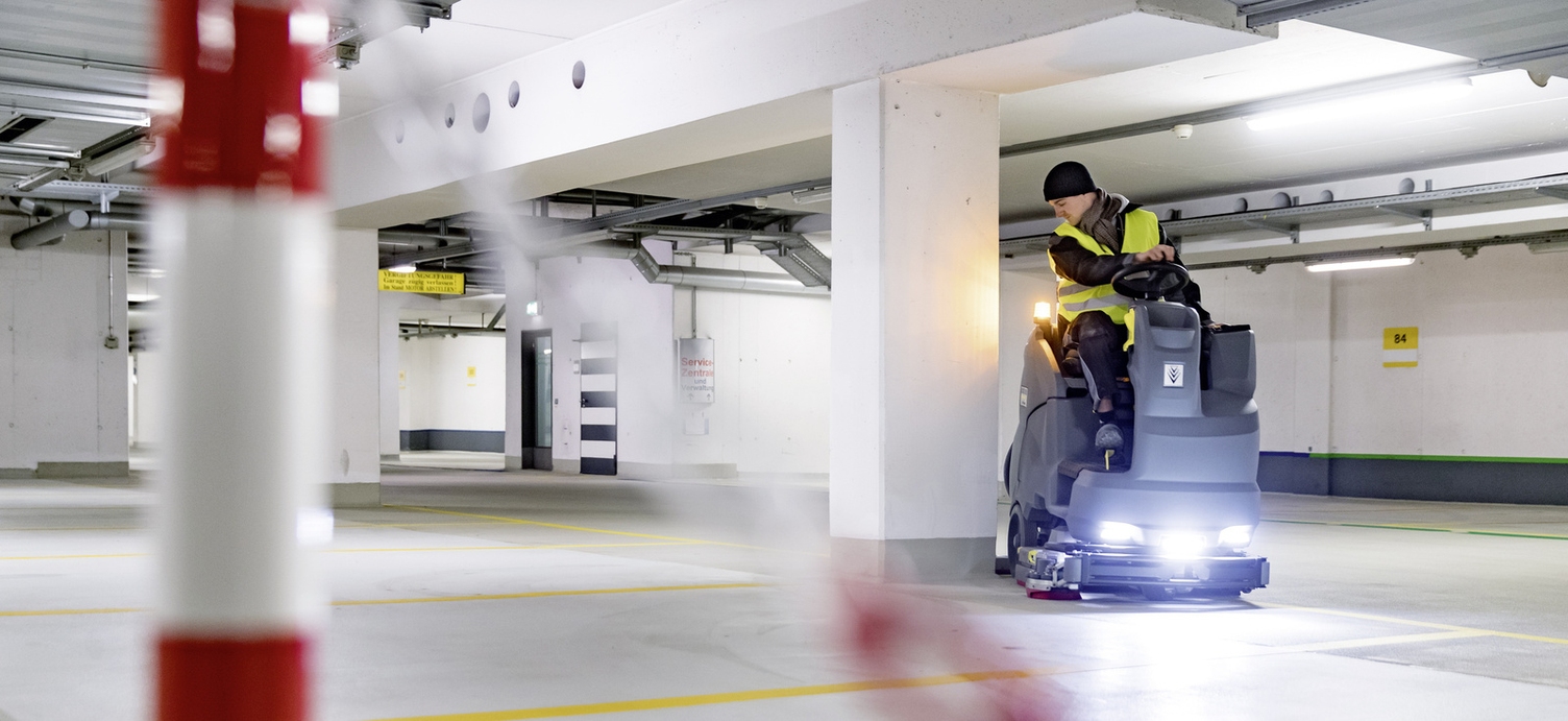 A person sitting on a ride-on sweeper cleaning an airport area