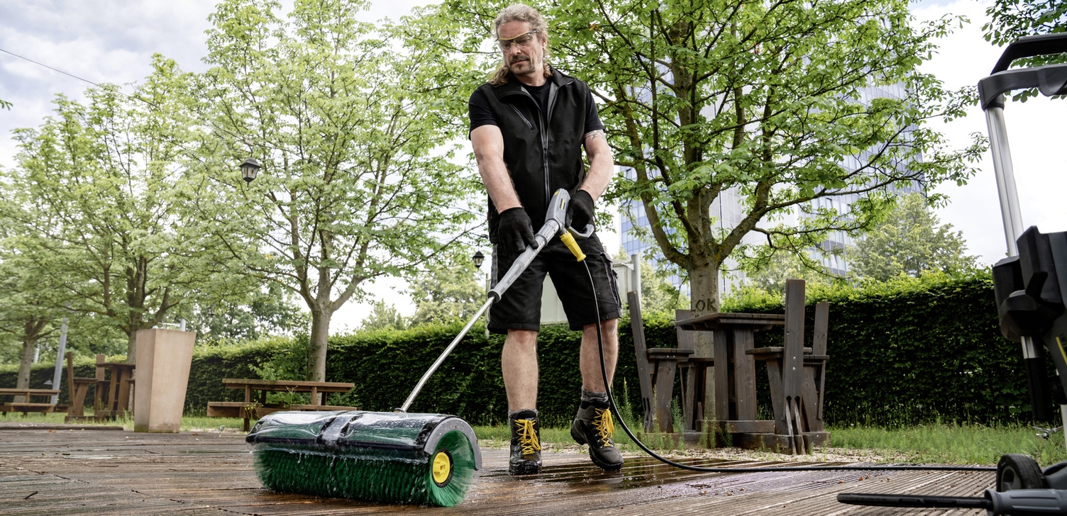 A person cleaning the wooden floor of a terrace with a Kärcher facade cleaning system