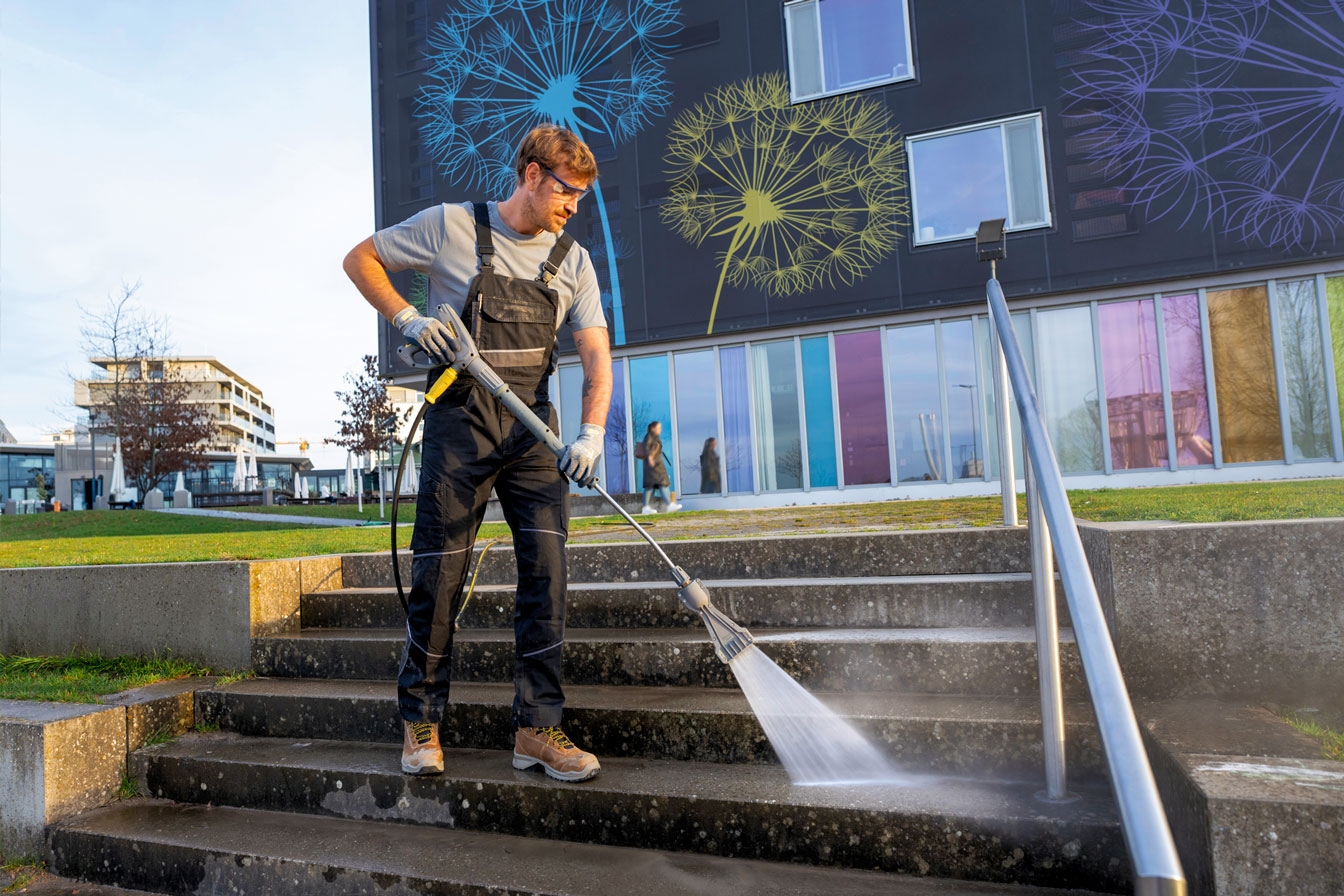 A worker pressure washes public steps using a hot water pressure washer.