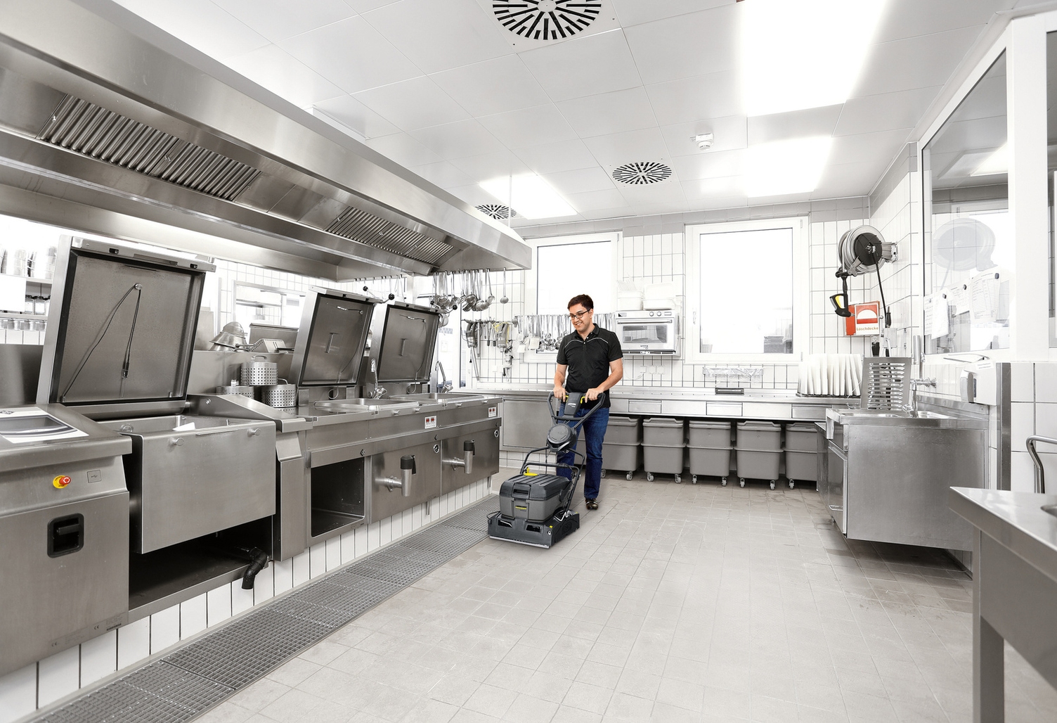 A person cleans the floor of a commercial kitchen with a surface cleaner