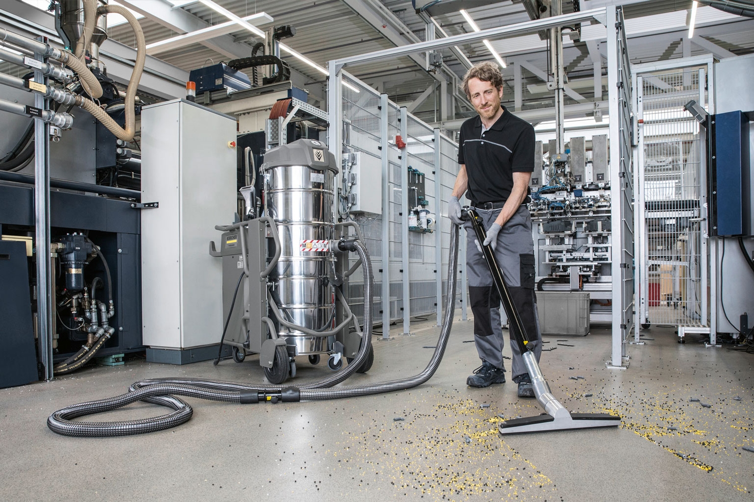 A worker cleans floors in a production facility using an industrial vacuum.