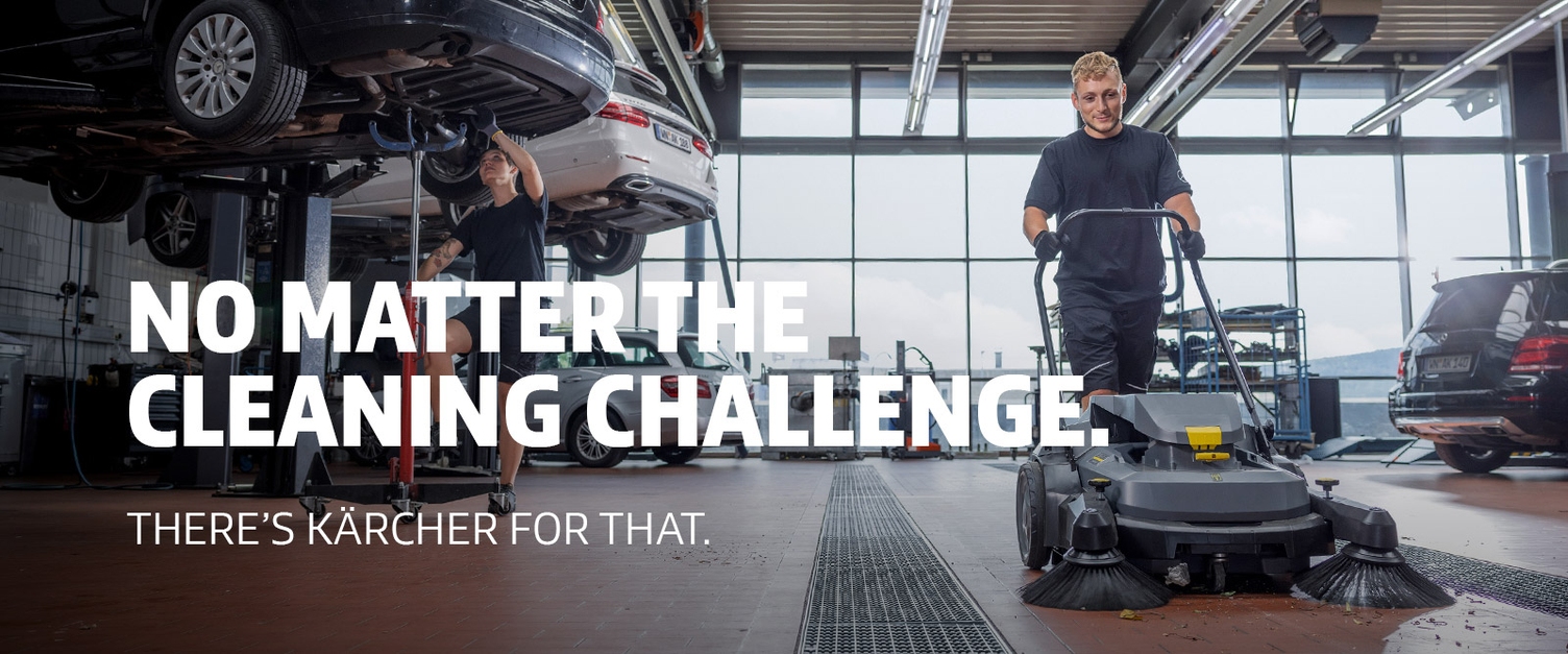 A worker uses a Kärcher KM 70/30 walk-behind sweeper in an auto service center.