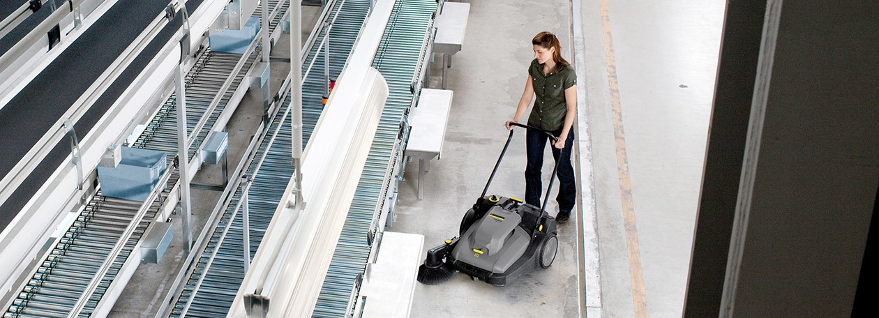 Commercial Floor Sweeper Rentals A worker uses a walk-behind floor sweeper to clean floors in a manufacturing facility.