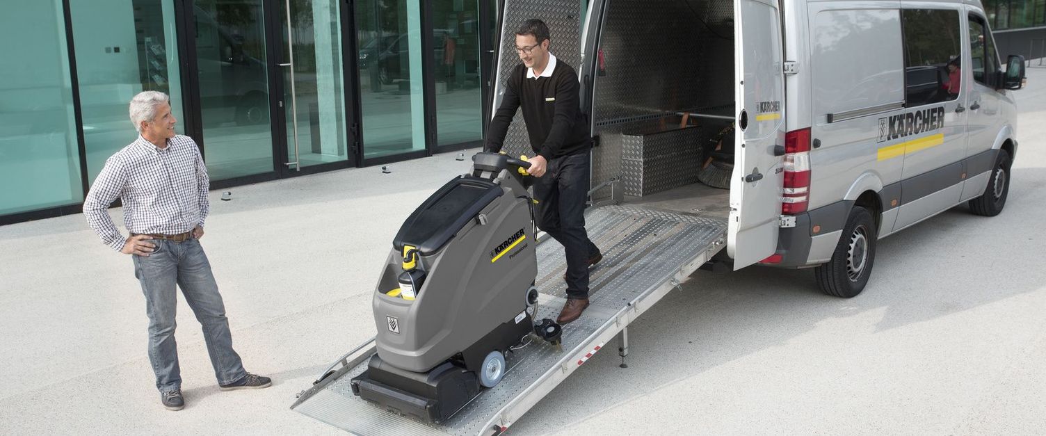 A Kärcher representative removes a walk-behind floor scrubber from the back of his service van.