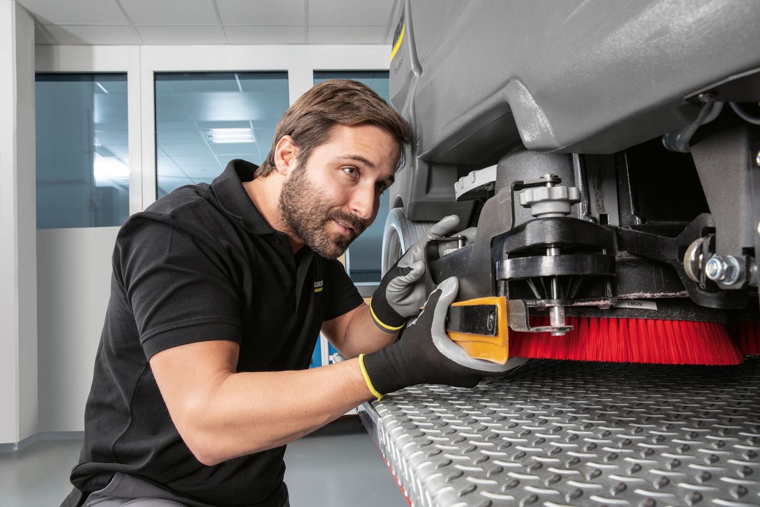 A Kärcher service technician inspects the underside of a floor scrubber.