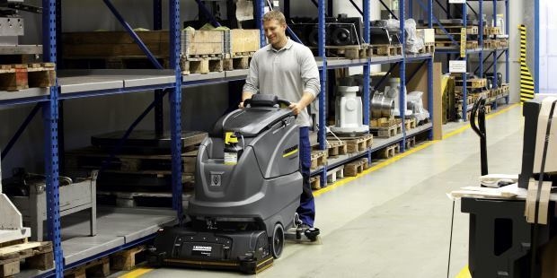 A man uses a floor scrubber in a manufacturing facility.