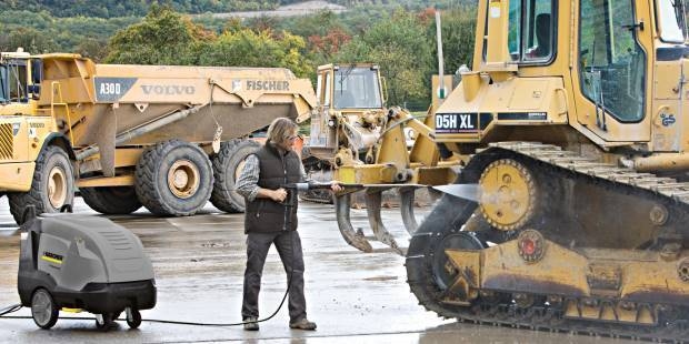 A worker pressure washes heavy construction equipment.
