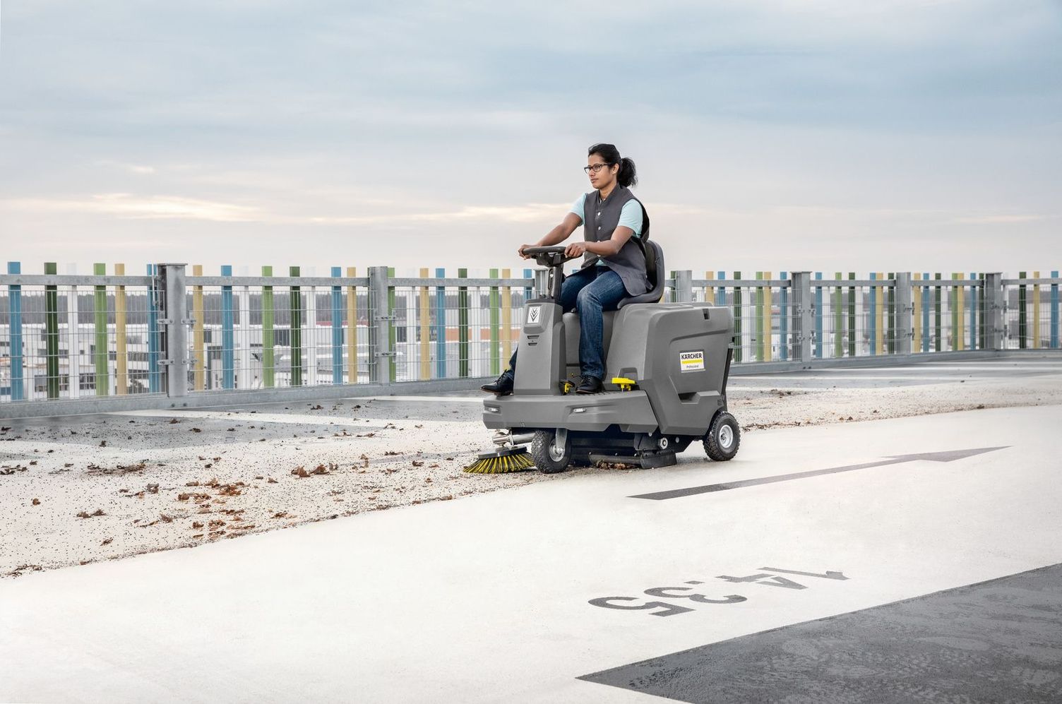 Woman sitting on a Kärcher ride-on floor sweeper.