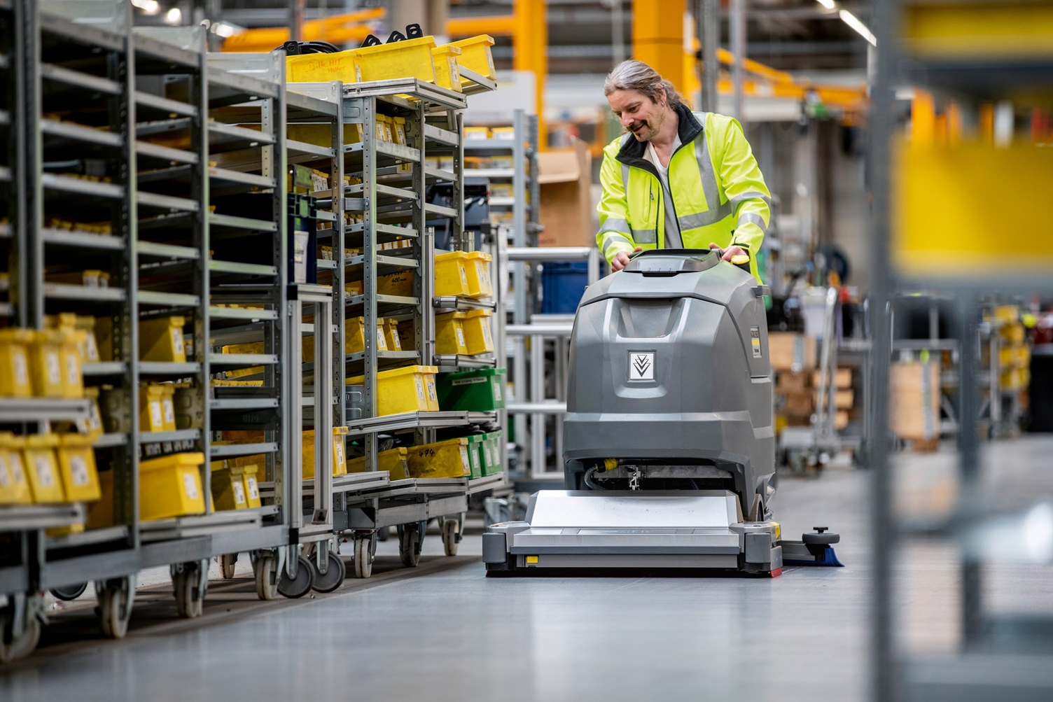 A worker uses a walk-behind floor scrubber to clean manufacturing center floors