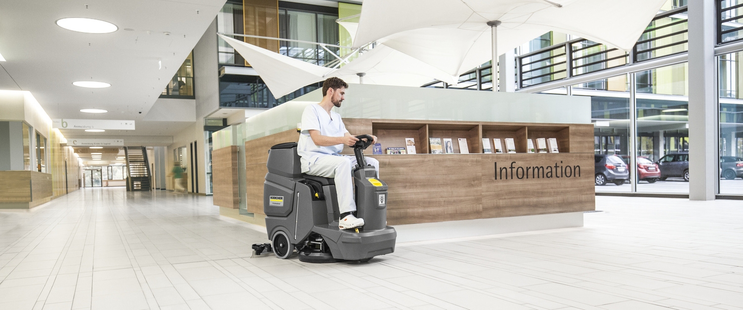 Prerequisite No. 1: Structural Quality A person cleans floors in the reception area with a Kärcher ride-on sweeper.