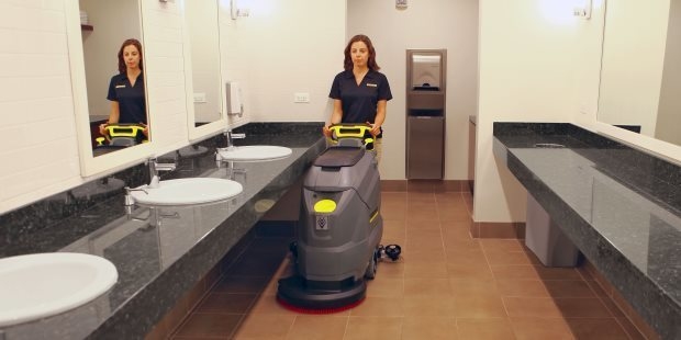 Restrooms A woman cleans a school restroom with Kärcher BD 50/50 walk-behind floor scrubber.