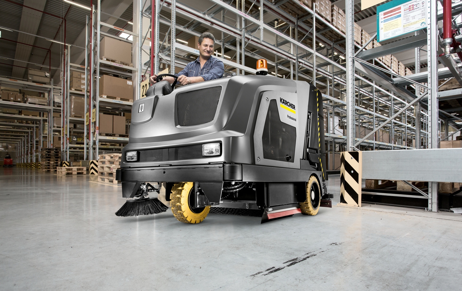 A dramatic image of a worker using a ride-on scrubber in a warehouse.