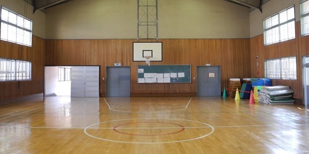 Gymnasiums & Pools An empty gymnasium with clean floors and a basketball hoop.