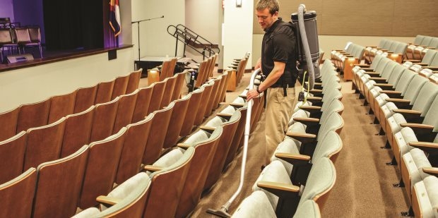 Theaters & Music Halls A worker cleans a school theater with a backpack vacuum.