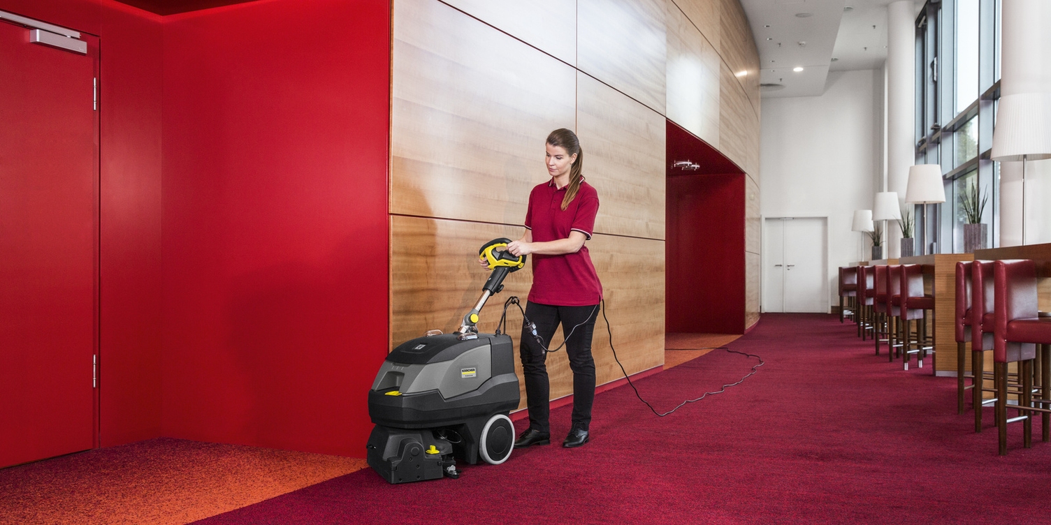 A worker cleans red carpets in a hotel hallway.