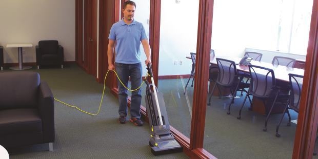 A worker vacuums carpets with a Kärcher upright vacuum cleaner.