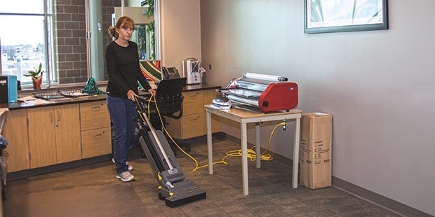 Offices & Lounges A worker vacuums a school office with an upright commercial vacuum cleaner.