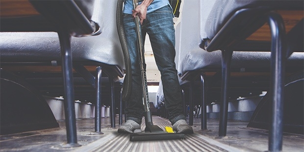 Buses & School Bus Depots A worker vacuums floors on a school bus.