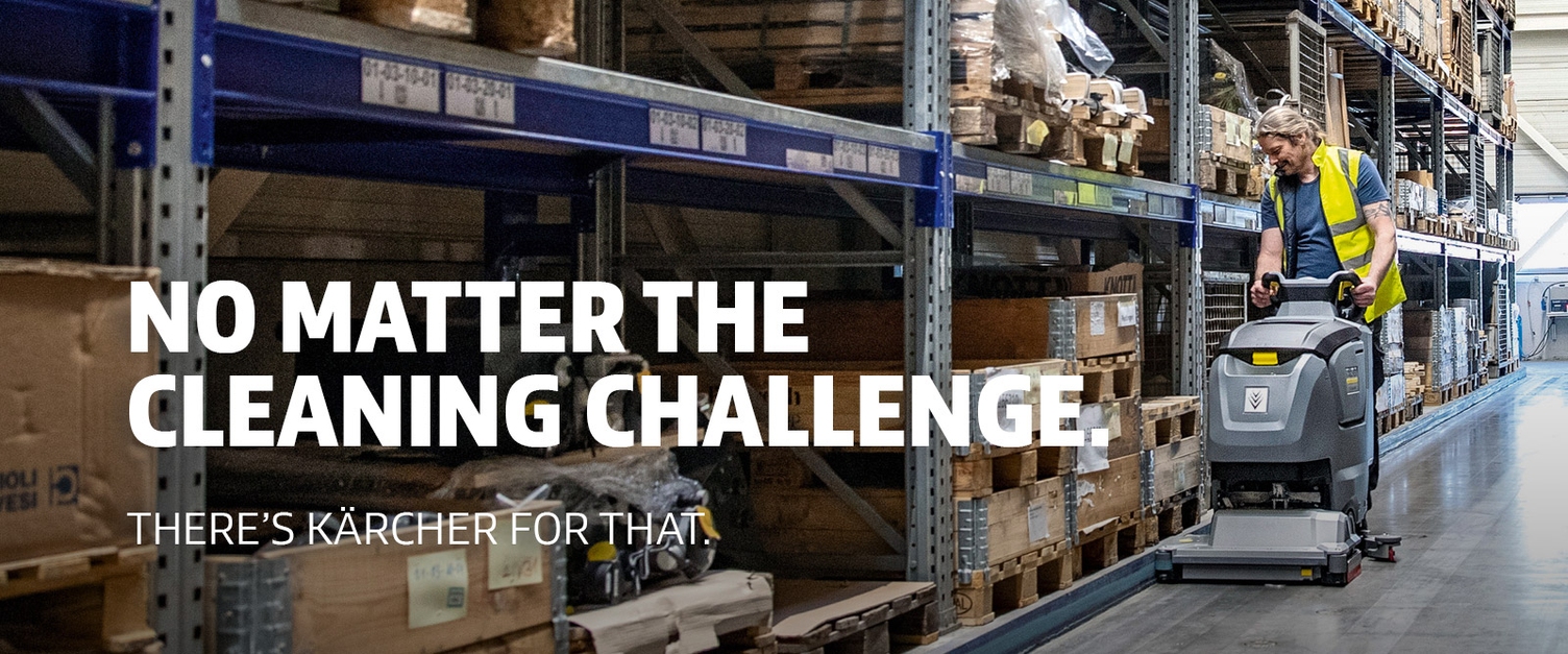 A man uses a walk-behind floor scrubber to clean warehouse floors.