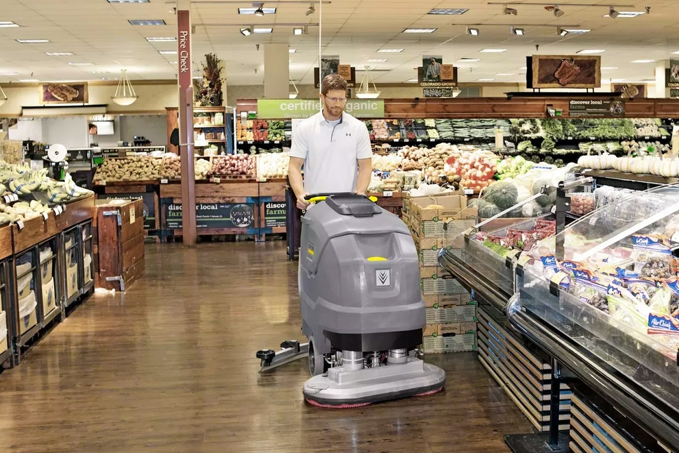 A worker cleans floors in a grocery store with a BD 80/100 Walk-Behind Floor Scrubber.