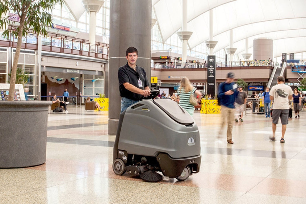 A worker uses a Chariot™ stand-on floor scrubber to clean airport terminal floors