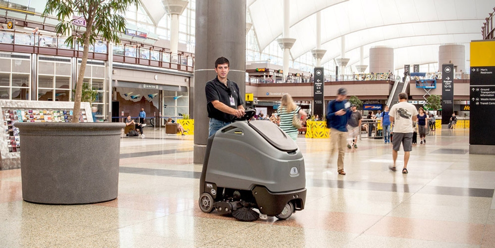 A worker uses a Kärcher commercial stand-on floor scrubber in an airport terminal.