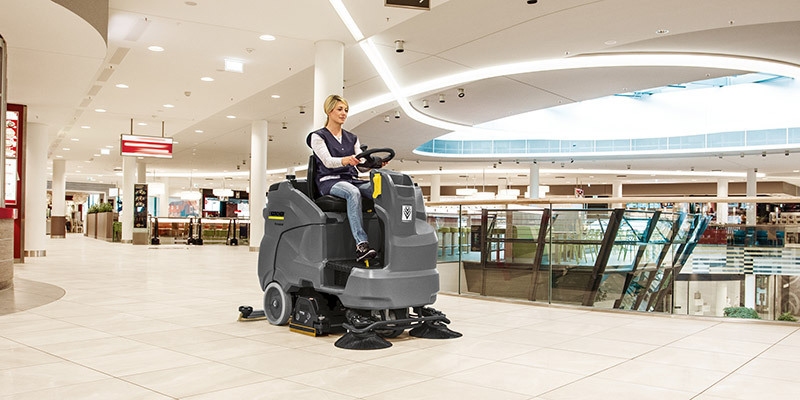 Cleaning in Shopping Centers & Retail Environments A worker cleans large floor areas using a ride-on floor scrubber
