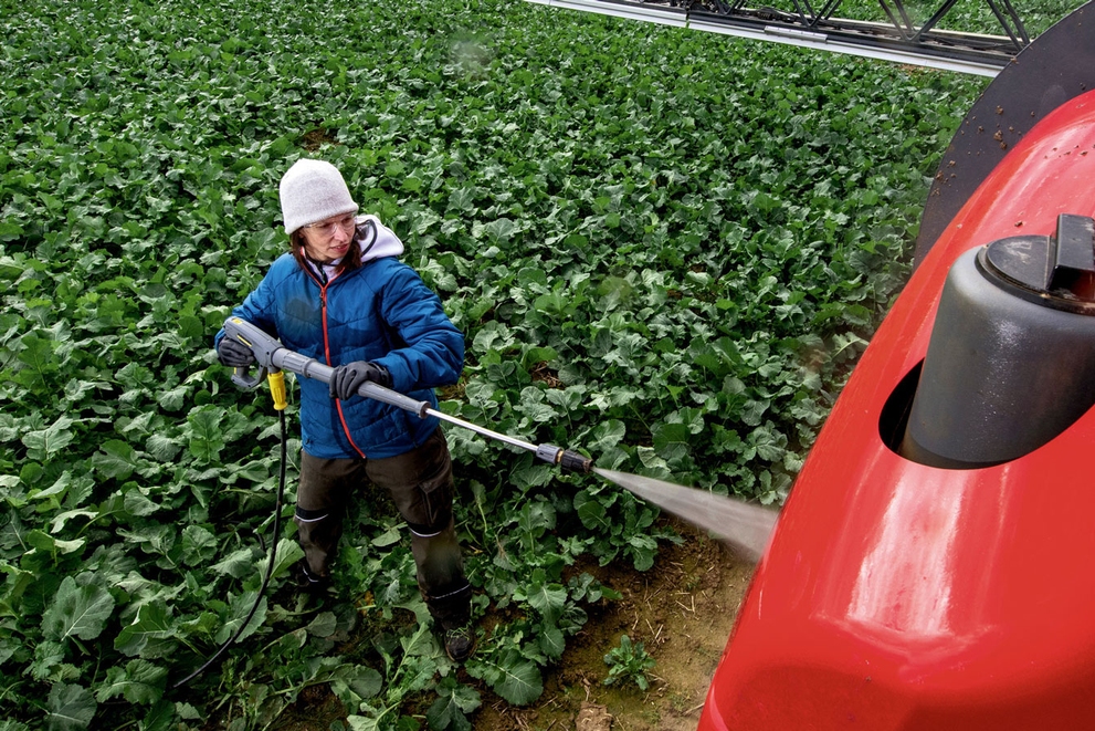 Cold Water Battery-Powered Pressure Washers A worker cleans agriculture equipment in the field with a battery-powered cold water pressure washer.