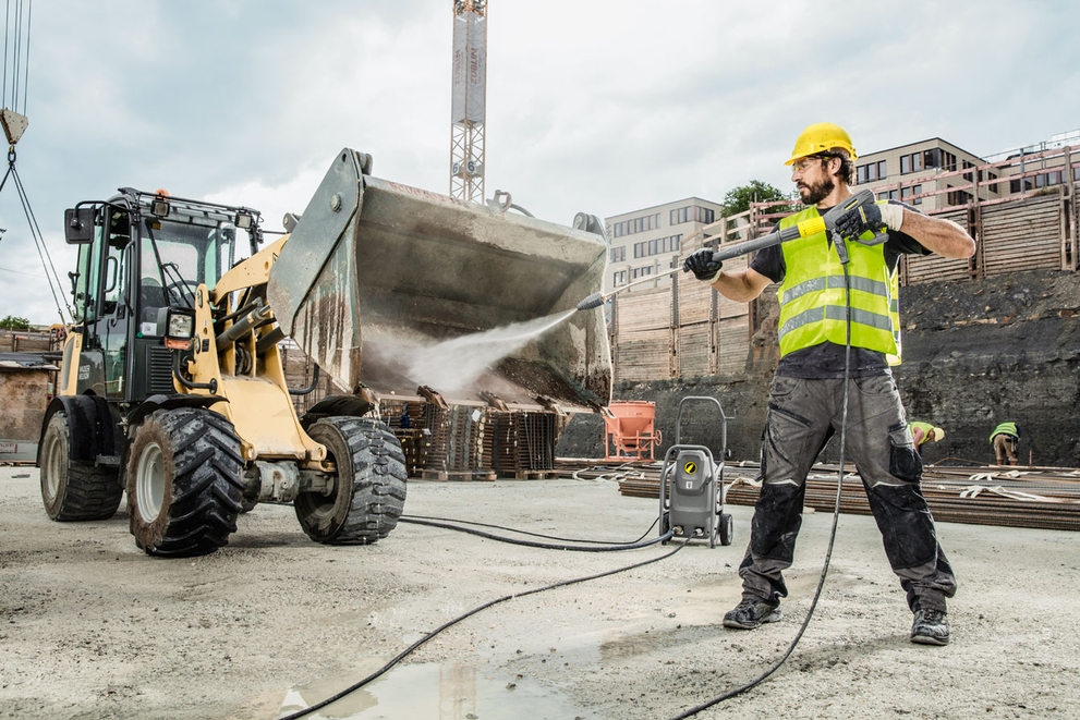 A worker pressure washes construction equipment using a cold water pressure washer.