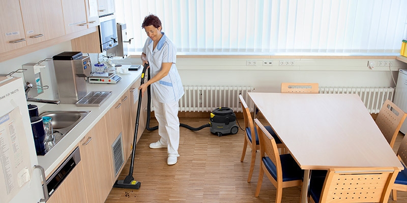 A worker uses a Kärcher commercial canister vacuum in a medical facility.