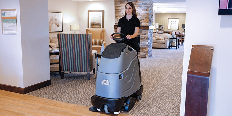 A worker uses a Kärcher commercial stand-on vacuum in a senior living facility.