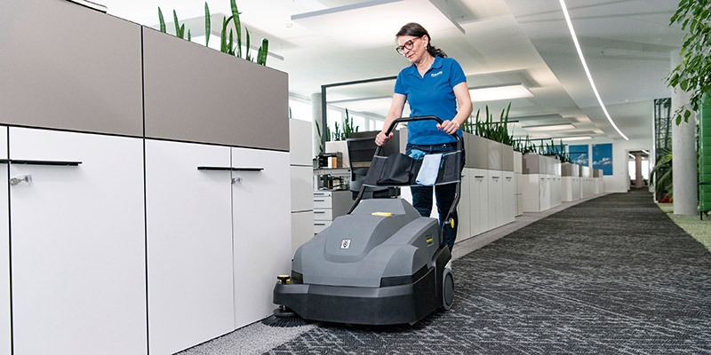 A worker vacuums inside an office building with a Kärcher commercial upright vacuum.