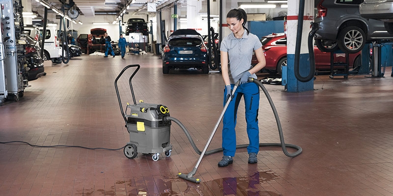 Auto shop worker cleans a spill with a Kärcher commercial wet dry vacuum.