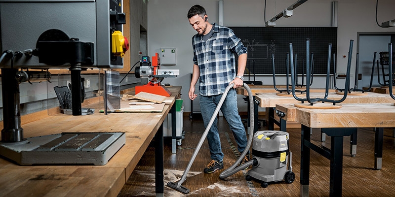 A worker uses a Kärcher commercial wet dry vacuum to collect dust on a shop classroom floor.