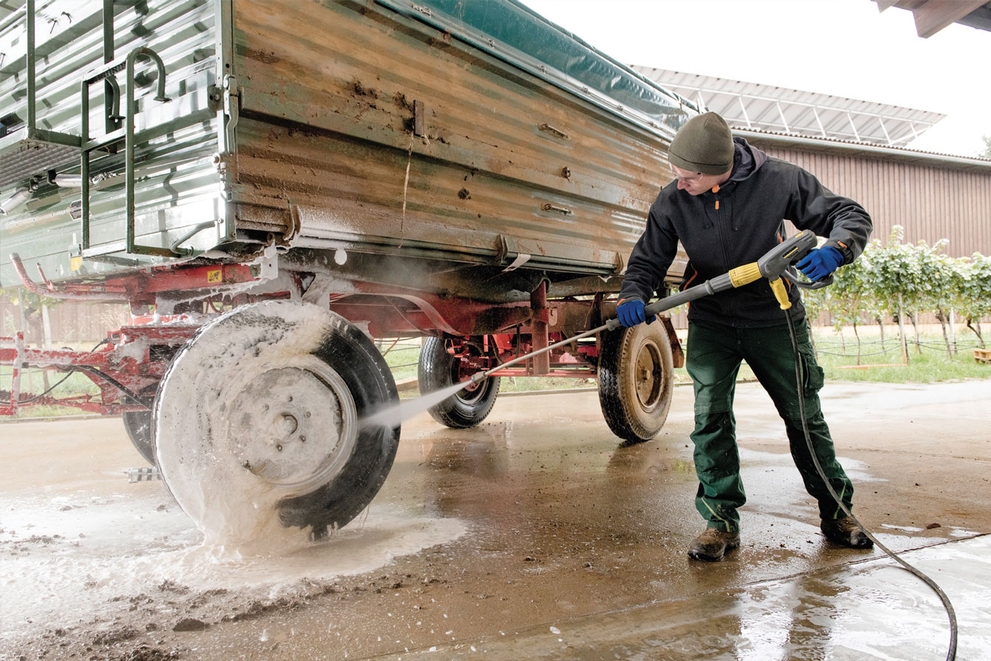 A worker cleans the back tires of agriculture equipment with a gas-powered cold water pressure washer.