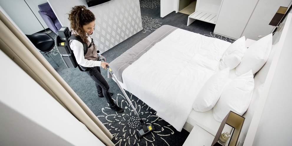 Cleaning Hotel Rooms With a Backpack Vacuum A hotel worker cleans a bedroom with a backpack vacuum cleaner.